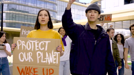 Young-Woman-Holding-Environment-Board-While-Her-Friend-Raising-Up-His-Fist-En-Protest-Mode