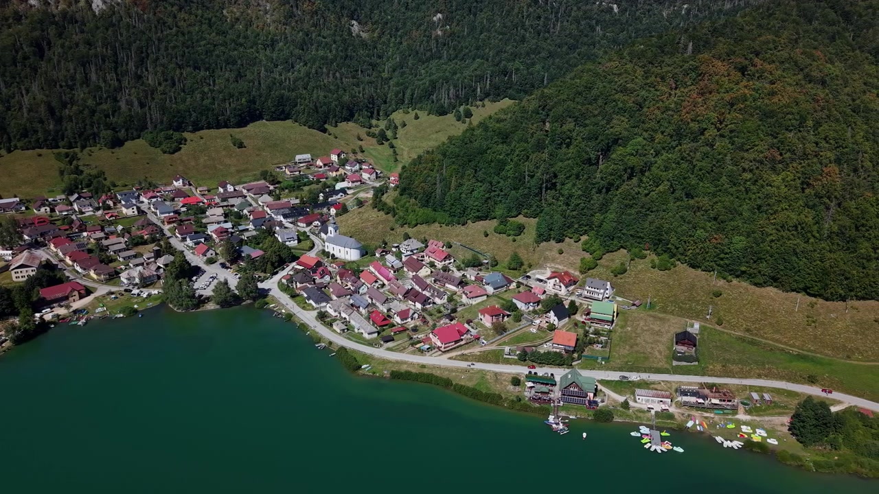 Een Luchtfoto Toont een Schilderachtig Dorp Gelegen Naast een Levendig Groen Meer, met op de Achtergrond een Dicht Bos en Bergen