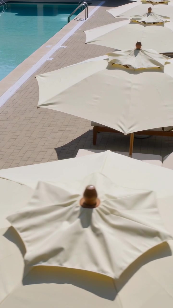 Vertical video: Panning camera showing cream parasols, padded loungers and pool ladder by deck