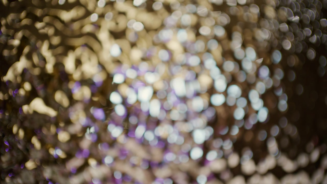 Abstract close up of golden, white, and purple bokeh lights with a soft glittering texture