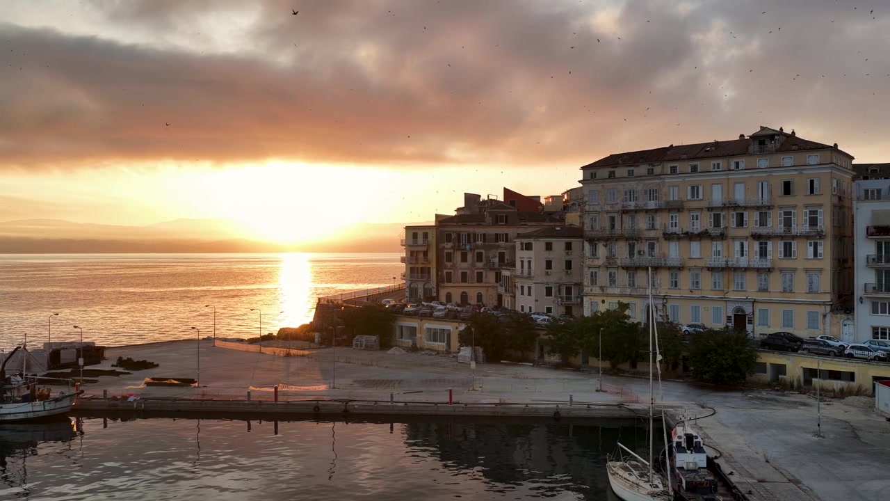 Splendida alba dorata sul vecchio porto dell'isola di Corfù in Grecia. Vista panoramica suggestiva con una nave da crociera che arriva all'alba, edifici veneziani storici, uccelli in volo e mare Mediterraneo calmo
