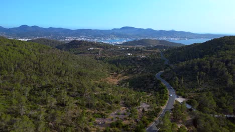 road winding through a vibrant green forest in ibiza, spain, leading down towards the beautiful san antonio bay. fantastic aerial view flight overflight flyover drone