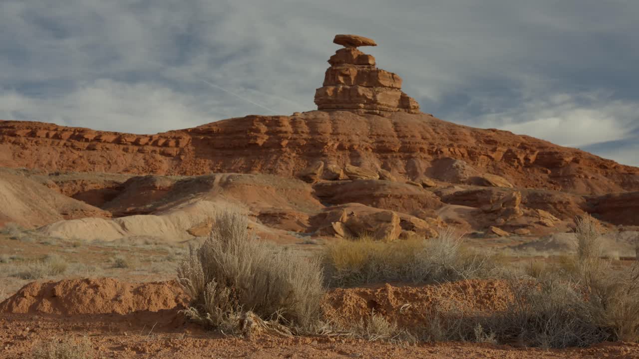 Cinematic left to right dolly shot of Mexican Hat Monument, a famous desert rock formation in Utah. Scenic red rock landscape showcasing iconic geology and American Southwest scenery