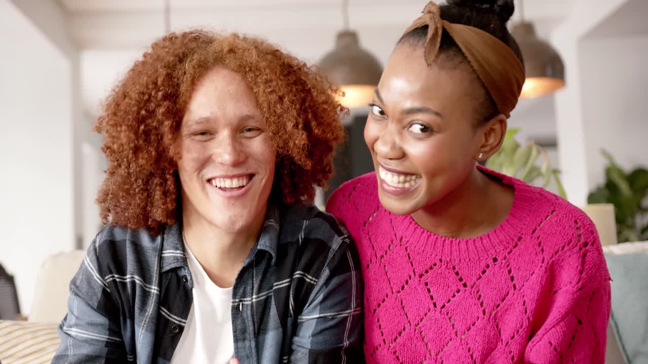 Happy diverse couple making video call sitting on sofa talking in living room, slow motion