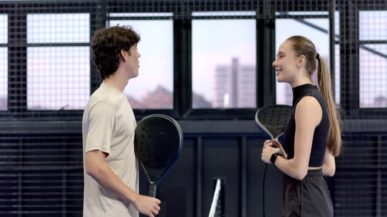 Young adults discussing padel tennis strategy on indoor court, holding racket and ball