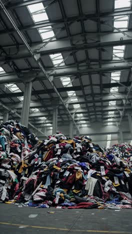 wide-angle shot of towering clothing piles in a warehouse, highlighting fast fashion waste