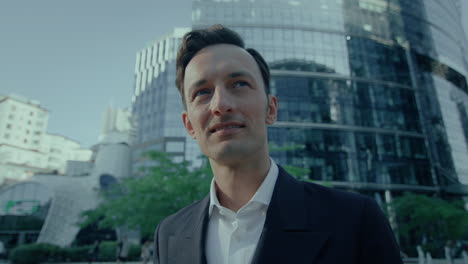 portrait of handsome business man in suit smiling and looking aside outdoors at financial district