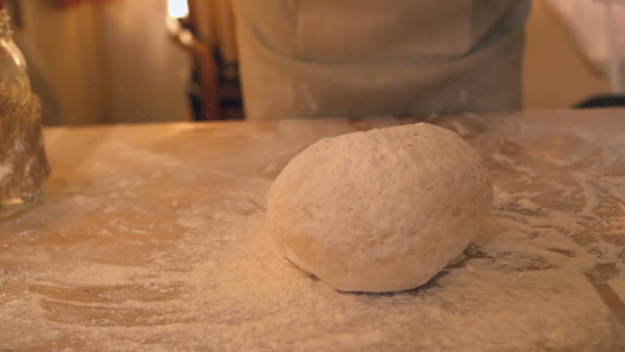 Hands dropping ball of dough onto floury surface