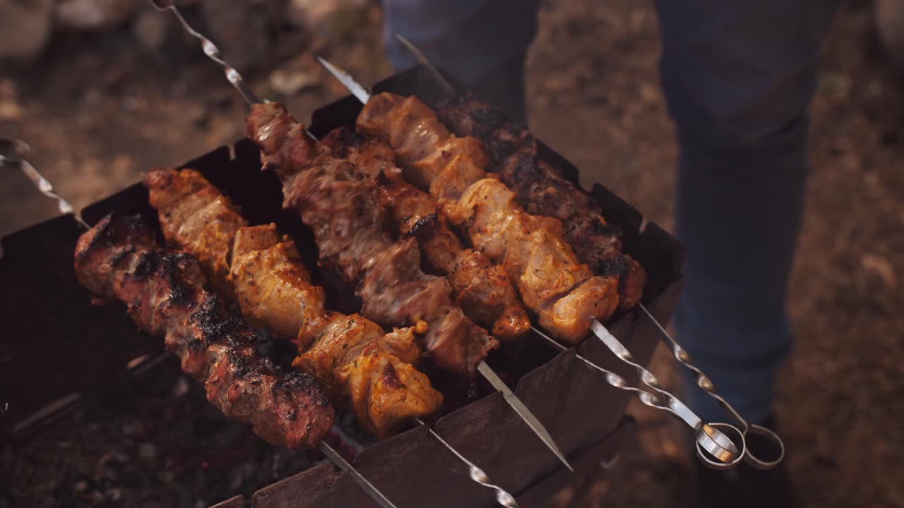 Male hand grilling meat on outdoor grill. Cooking meat barbecue on charcoal grill at picnic.