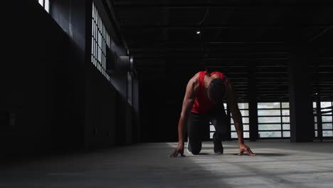 african american man kneeling starting a run in an empty building