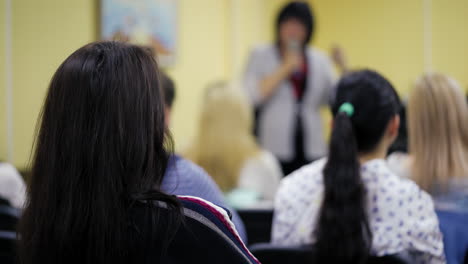 back view of dark-haired female sitting in the conference hall on the blurred background. young ladies sit and listen carefully to business training on women's development.