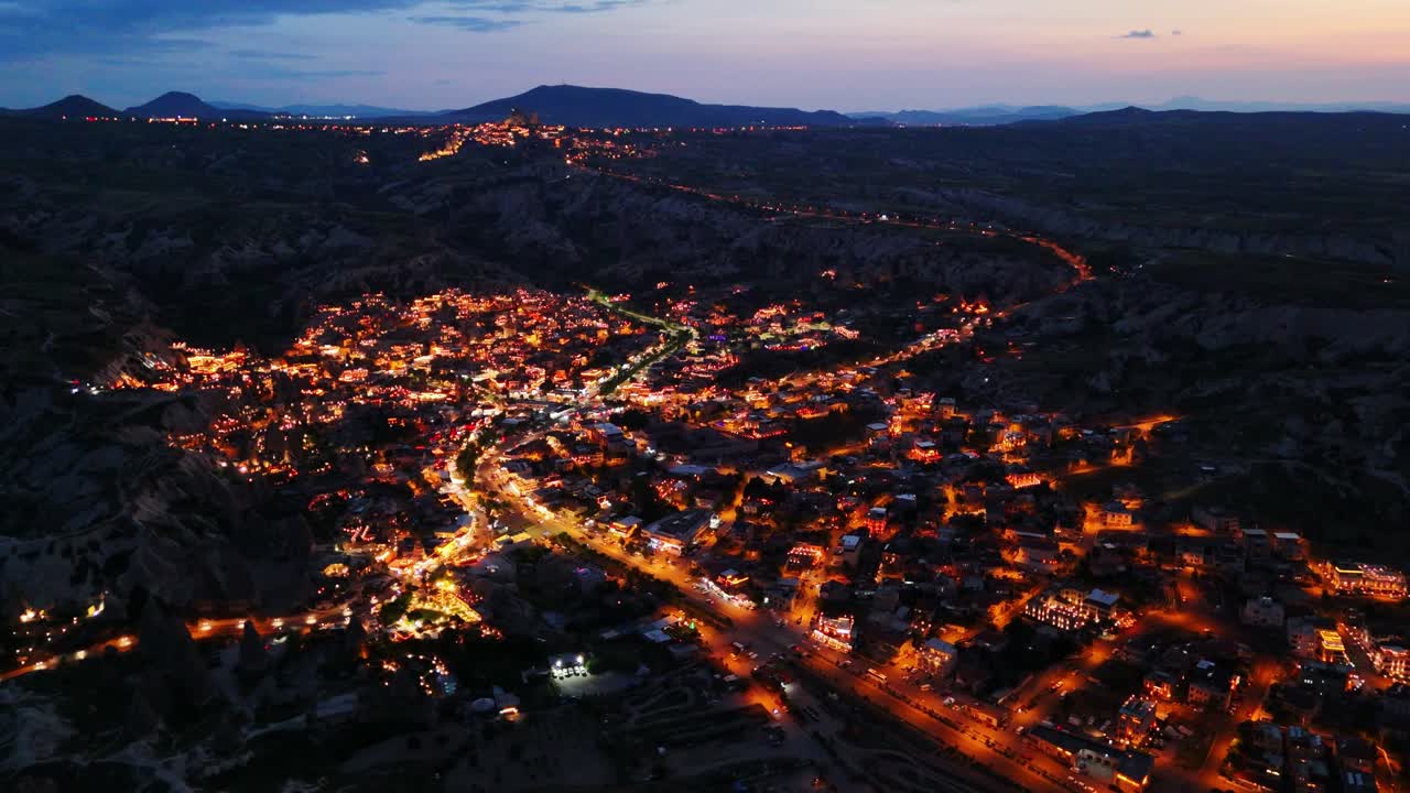 Aerial night view of a glowing cityscape and distant mountains