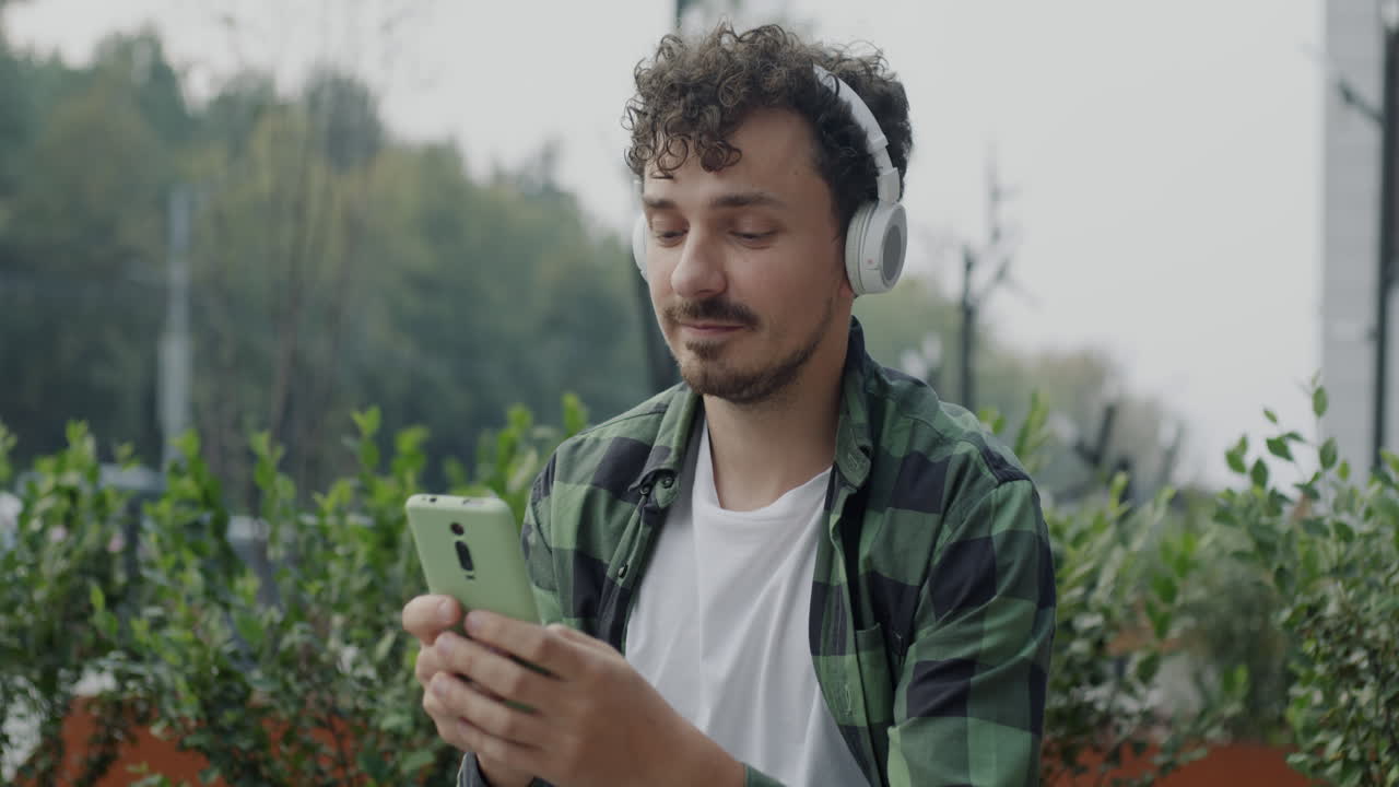 Young Man Listening to Music and Using a Smartphone Outdoors