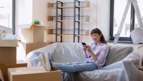 Happy-Woman-Calling-on-Phone-Moving-to-New-Home.moving,-people-and-real-estate-concept--happy-smiling-asian-woman-with-boxes-calling-on-smartphone-at-new-home