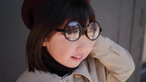 korean girl in a gray coat and cap stands the street in spring at the glass doors of the store