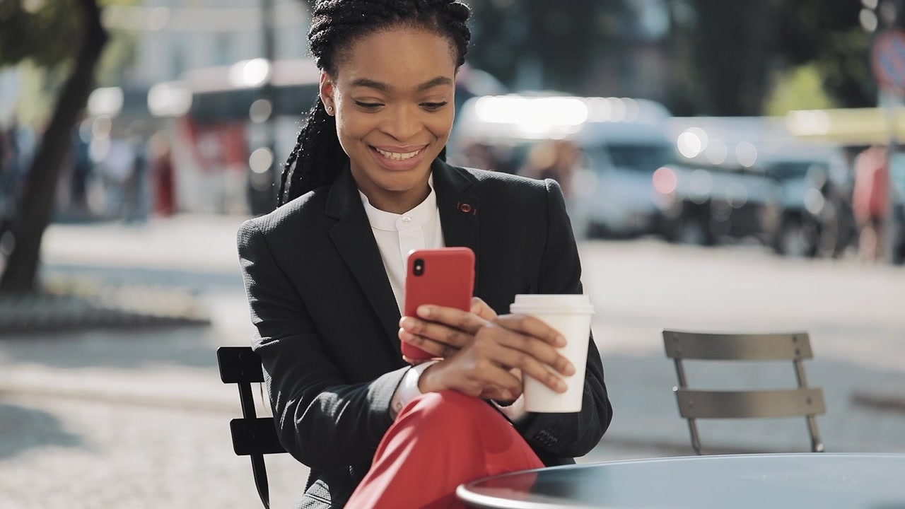 Smiling Businesswoman Using Smartphone and Drinking Coffee at Outdoor Cafe