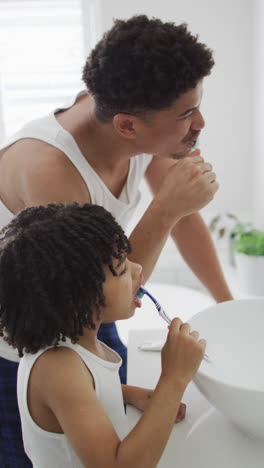 video vertical de un padre biracial feliz con su hijo cepillándose los dientes en casa