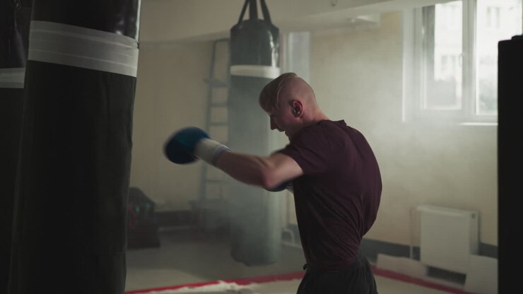 Boxer punches heavy bag exercising in sports center. Emotional athlete in gloves beats hanging item by fists in gym slow motion. Relax technique