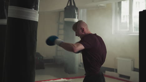 boxer punches heavy bag exercising in sports center. emotional athlete in gloves beats hanging item by fists in gym slow motion. relax technique