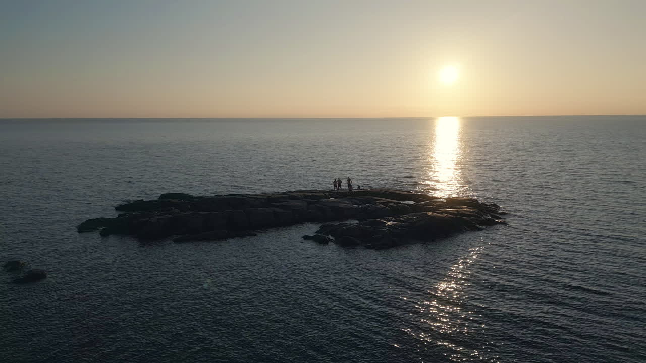 바위 섬에 서서 해가 지는 평온한 바다를 바라보는 사람들