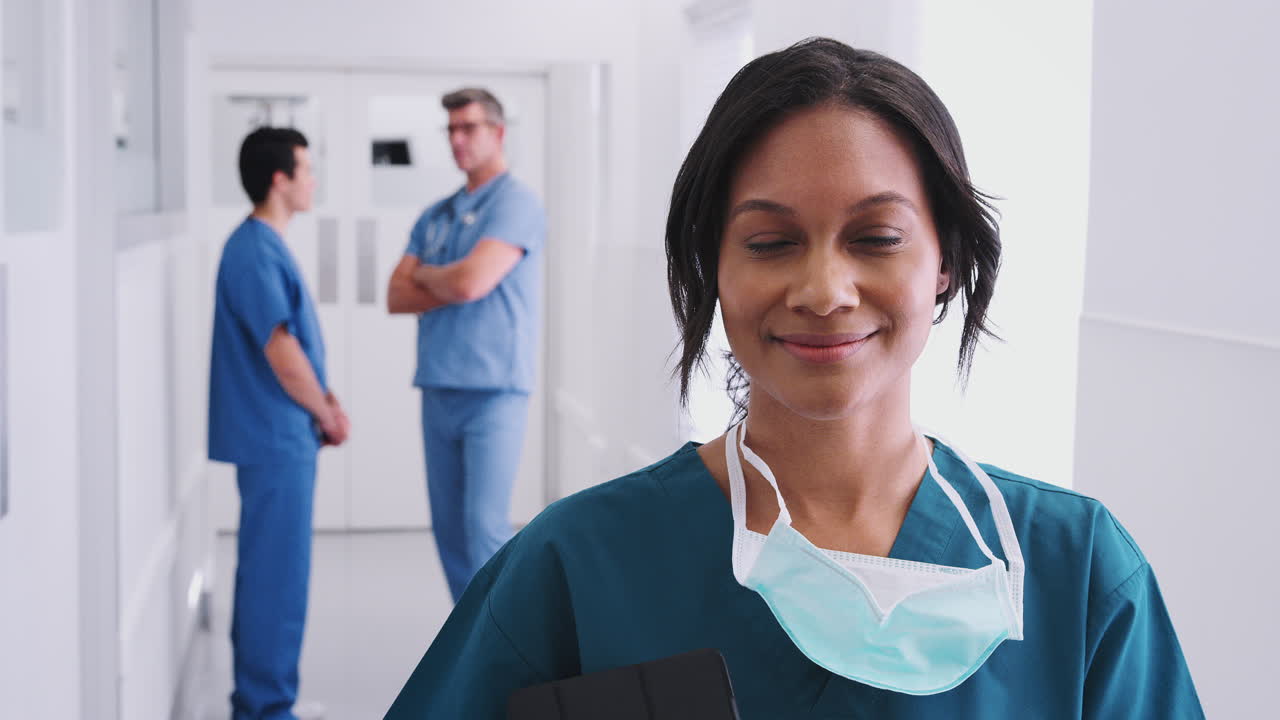 cirujana vestida con exfoliantes y máscara en un concurrido corredor del hospital con colegas en el fondo