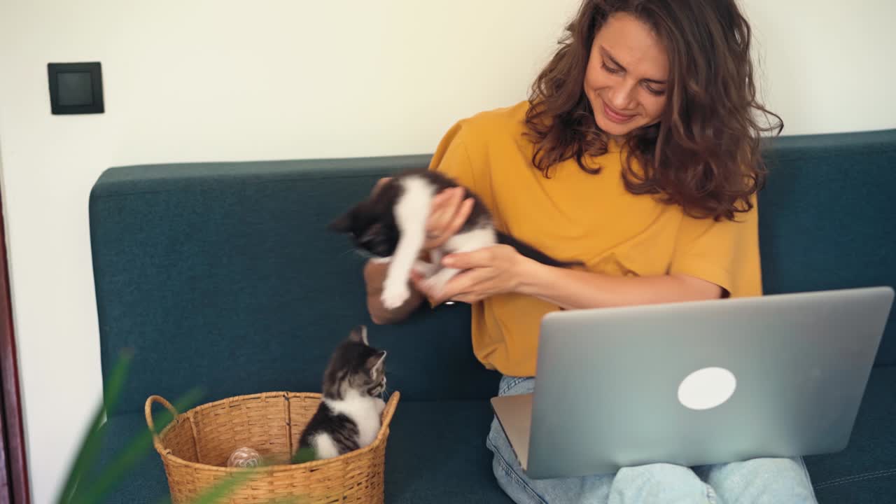 una mujer joven jugando con dos gatitos pequeños mientras trabaja desde casa
