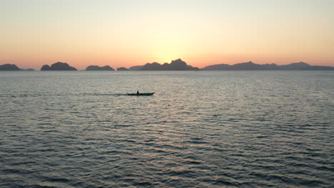 Antena-Que-Muestra-Un-Barco-De-Pesca-De-Madera-Cruzando-Con-La-Puesta-De-Sol-En-El-Fondo-En-El-Nido,-Palawan,-Filipinas