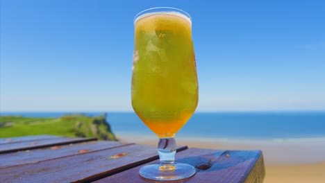 low angle view of cooled lager beer in glass standing on picnic table overlooking sea with sandy beach and cliffs. chilled alcoholic drink. example of holiday vacation rest and relaxation.