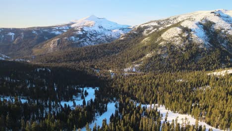 drone birdseye footage over ski slopes and surrounding alpine forest on a clear and sunny winter's day, moving forward towards snowcapped mountains in lake tahoe, usa