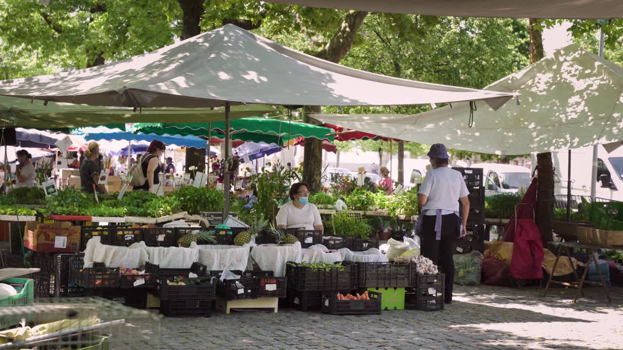Wide shot of two farmers wearing masks and selling their vegetables in a fair, after the end of lockdown (deconfinement), in Barcelos, Portugal.