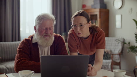 Senior Man Using Laptop at Home with Help from Young Daughter