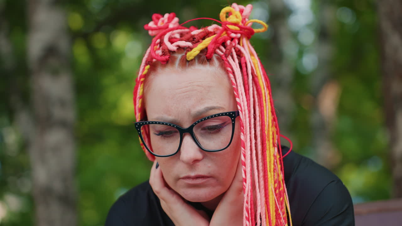 반사적인 여성 관찰자, 다채로운 땋은 머리를 한 생각에 잠긴 여성, 생생한 땋은 머리를 하고 공원 벤치에 앉아 있는 사색에 잠긴 여성, 선명한 머리 색깔에 큰 안경을 쓴 사려 깊은 여성