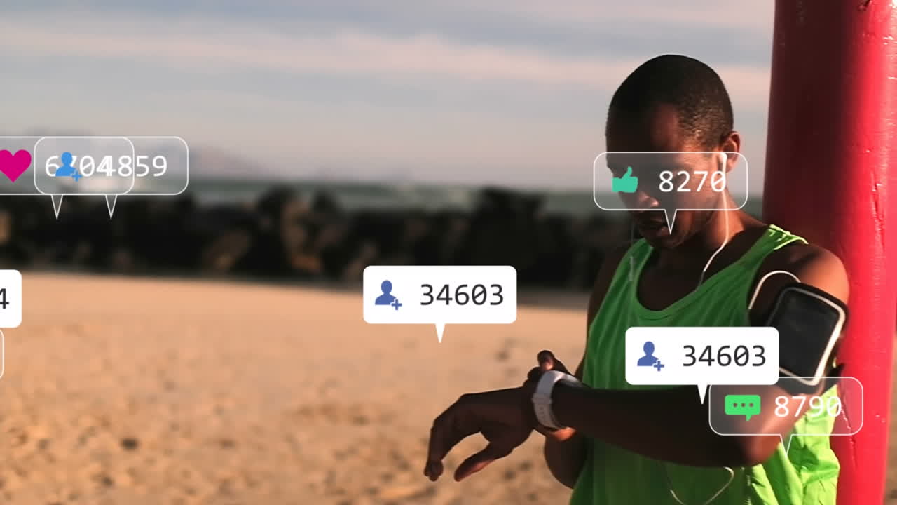 Animazione di icone di social media su un uomo afroamericano in forma che usa uno smartwatch in spiaggia