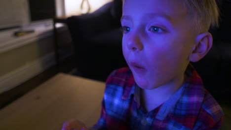 close-up of a little boy's face as he watches tv and eats popcorn