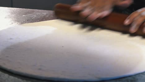 Close-Interior-Static-Shot-of-a-Chef-Rolling-out-Pizza-Dough-With-Wooden-Rolling-Pin-and-Patting-it-Down-With-Plastic-Pot-in-Pizza-Restaurant-at-Night