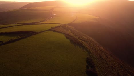 descending sunset aerial view over coastal fields in devon with bright setting sun flare and hazy background. drone rural farming footage 4k.