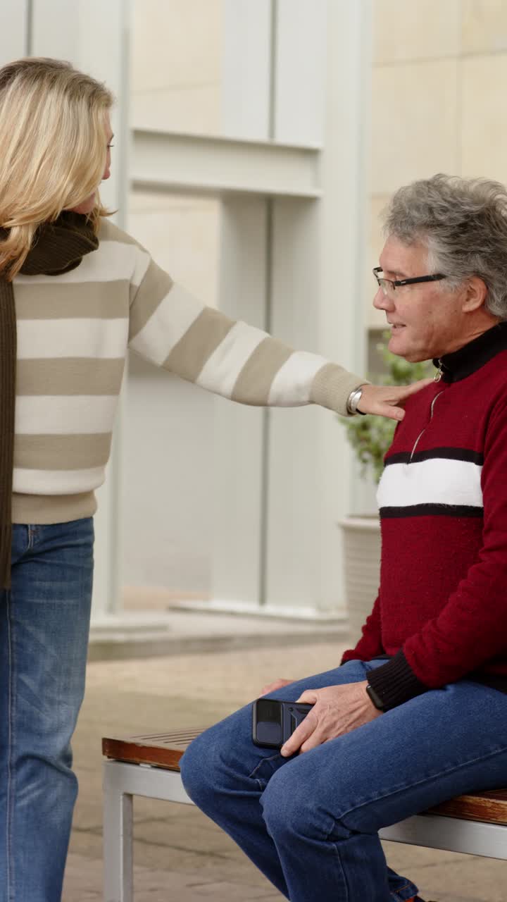 Vertical video: Couple on bench woman in scarf coming tapping man's shoulder pulling him from phone