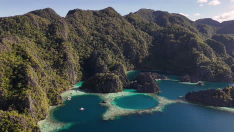aerial drone view of coron island’s dramatic cliffs, tropical greenery, and idyllic turquoise waters. boats anchored in the lagoons.