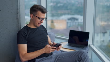man put away laptop he was working at. businessman in glasses typing something on his smartphone. close up. blurred backdrop.