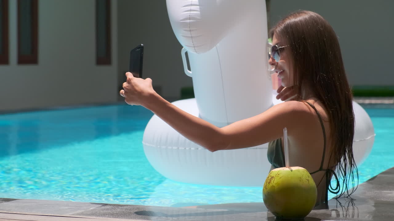 mujer tomando una selfie junto a la piscina con coco