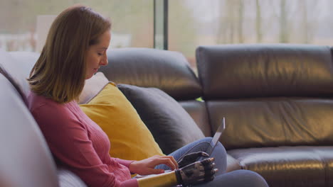 mujer con brazo y mano protésicos en casa trabajando en una computadora portátil