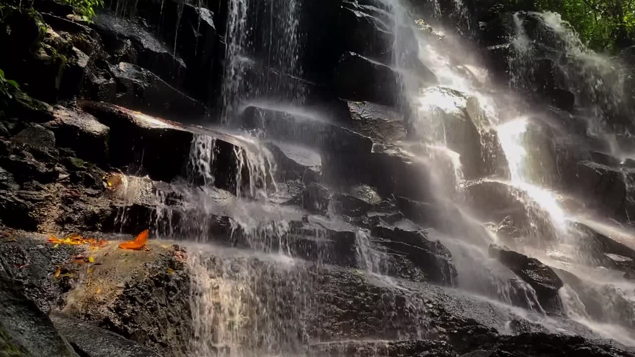 Beautiful Kanto Lampo Waterfall cascading over rocky steps, surrounded by lush greenery in Bali, static view of light shimmering on water