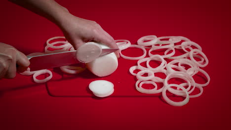 cocinera desconocida cortando cebollas en la mesa roja. mujer con las manos cortando cebollas