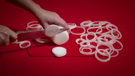 unknown female chef slicing onion on red table. woman hands cuttiong onion