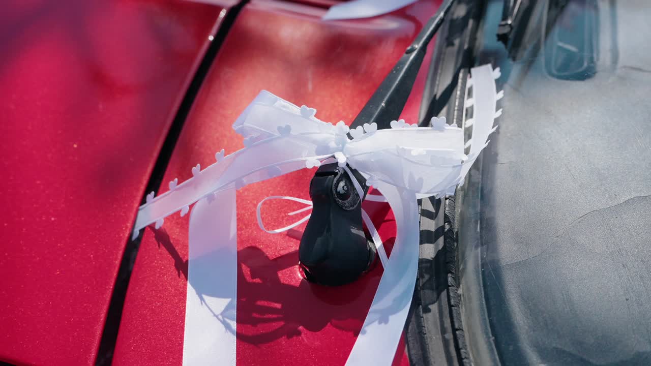 close up of white wedding ribbon tied to red car windshield and antenna in sunlight