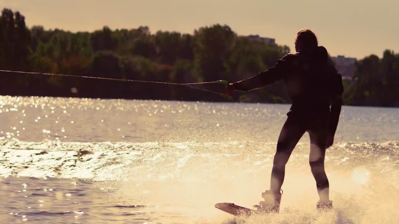 jinete de wakeboard moviéndose rápido en salpicaduras de agua en el atardecer dorado
