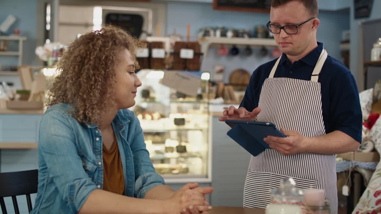 un camarero caucásico con síndrome de down discutiendo el menú con el cliente.