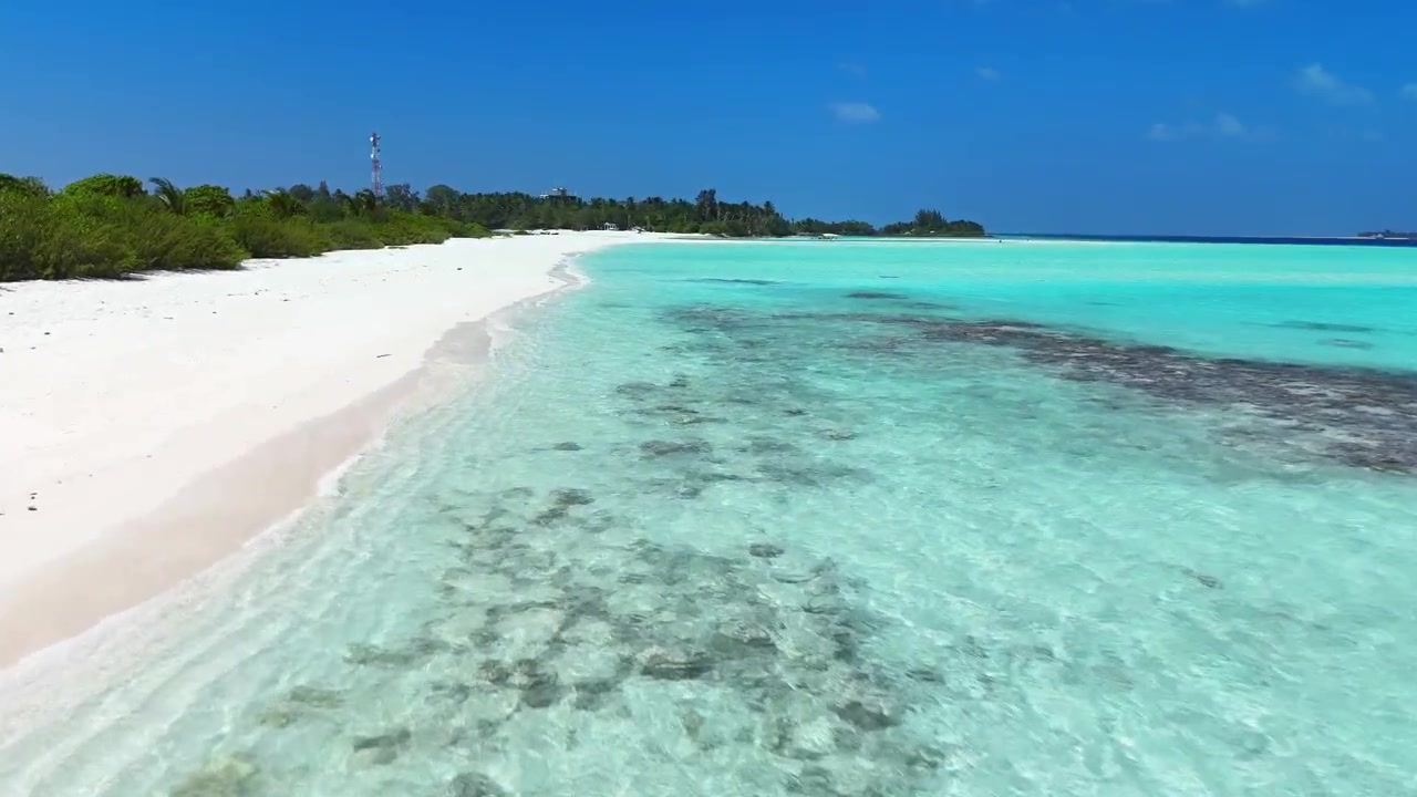 Ripresa aerea bassa con drone lungo la costa di una spiaggia di sabbia bianca con delicate onde turchesi alle Maldive