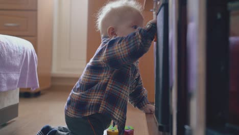 small-boy-nibbles-bright-toy-siting-on-floor-at-rack-in-room