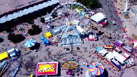 aerial-hold-top-view-worlds-largest-portable-Ferris-Wheel-at-150-feet-high-drone-overlooking-birds-eye-view-of-the-rides-line-ups-of-crowds-of-people-at-swings-go-karts-mega-drop-lots-more-fun-times